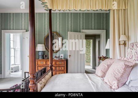 Hexagonal vintage mirror above wodden chest with four postered bed, view through doorways Stock Photo