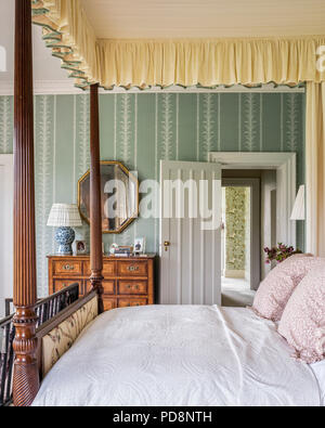 Hexagonal vintage mirror above wodden chest with four postered bed Stock Photo