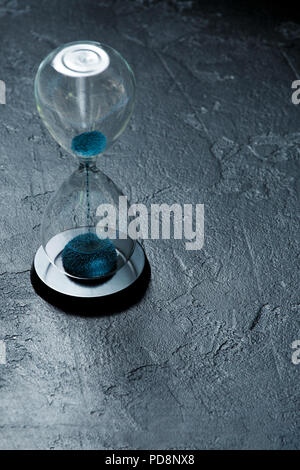 Photo of hourglass with blue sand on black stone background Stock Photo