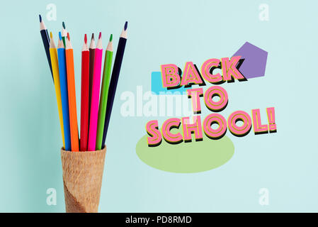 closeup of some pencil crayons of different colors in an ice cream cone and the text back to school on a green background Stock Photo