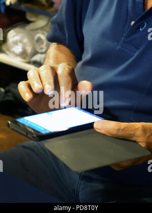 retired man using a smartphone indoors at night, seen typing on the touch screen. Stock Photo
