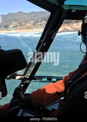 A Coast Guard aircrew circles above a lifeguard and a surfer in the water before hoisting the surfer onto the helicopter near Montara State Beach in Half Moon Bay, California, July 8, 2018, July 8, 2018. After the surfer became stranded on some rocks, the lifeguard helped the surfer swim into open water so the Coast Guard crew could conduct the hoist and transfer him to emergency medical services personnel waiting on shore. (Coast Guard courtesy photo/released). () Stock Photo