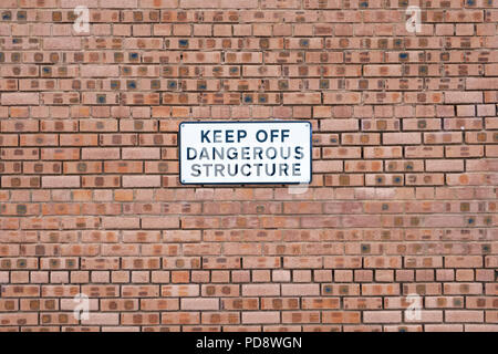 Keep off dangerous structure sign on plain orange brick wall Stock Photo