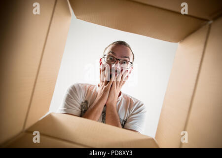 The surprised man unpacking, opening carton box and looking inside. The package, delivery, surprise, gift, lifestyle concept. Human emotions and facial expressions concepts Stock Photo