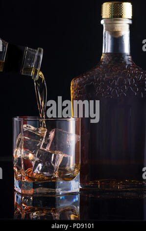 a glass of whiskey in which is poured with a bottle on a glass table Stock Photo