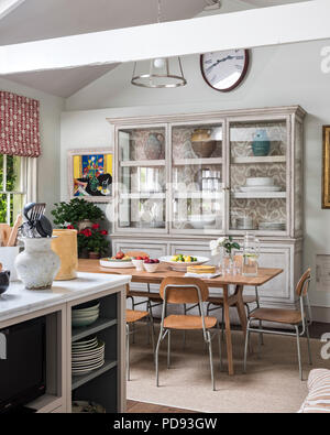 A large antique glazed cupboard in kitchen dining area. The dining table is from Made.com while the chairs are 50’s plywood. Walls painted in Paper an Stock Photo