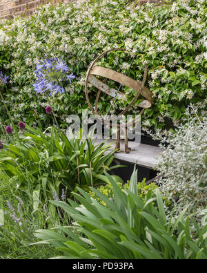 Rusty sculpture on garden ledge in amongst the agapanthus and jasmine Stock Photo