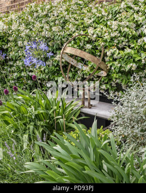 Rusty sculpture on garden ledge in amongst the agapanthus and jasmine Stock Photo