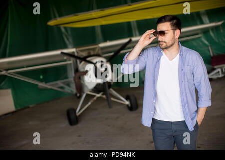 Young handsome young pilot checking airplane in the hangar and using mobile phone Stock Photo