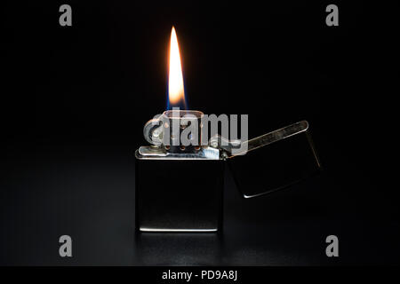 Shiny silver metallic lighter with lit flame of fire on a black background. Stock Photo