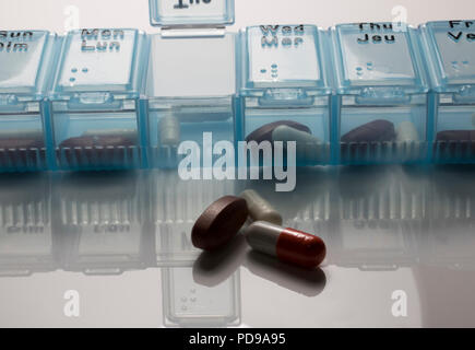 Blue Pill Dispenser with vitamins reflecting on a white table. Daily Dose of Medicine for the Elderly. Stock Photo