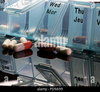 Close up of pills spilled out of a pill dispenser on a black table. Stock Photo
