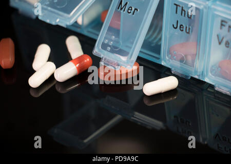 Dispenser spilling out drug capsules. Close up of Pills and vitamins coming out of a medicine dispenser on a black shiny surface. Stock Photo