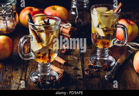 Two Glasses of Apple Mulled Drink with Clove, Cinnamon, Anise Star and Dark Candy Sugar. All Ingredients and Some Kitchen utensils on Wooden Table. Stock Photo