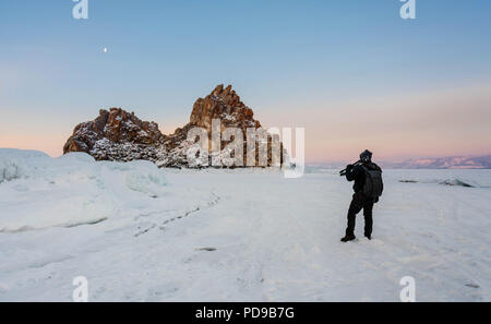 Travelling in winter, photographer carrying camera tripod at frozen lake Baikal in Siberia, Russia Stock Photo