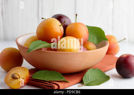 Fresh colorful plums in bowl on white stone background Stock Photo