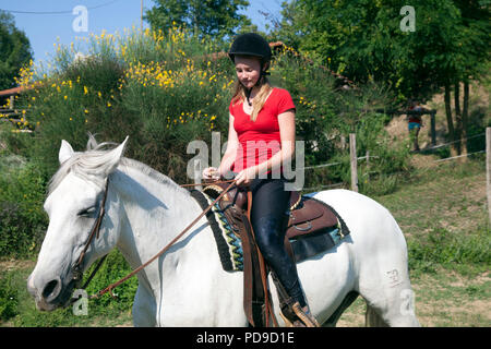 young teen girl in red shirt on white horse in green surroundings Stock Photo