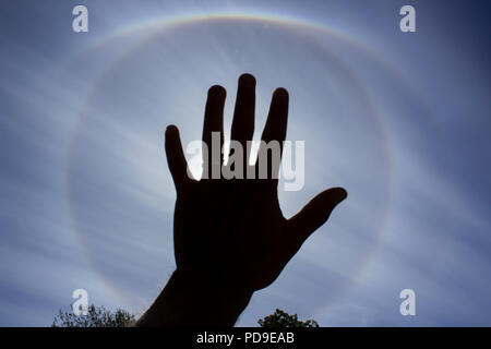 Stockholm, Sweden - August 6 2018: Circular rainbow around the sun which is blocked by the hand of a young male. Meteorological phenomenon. Stock Photo