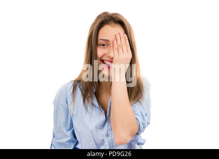 Pretty happy young brunette in blue shirt covering one eye and laughing at camera standing on white background Stock Photo