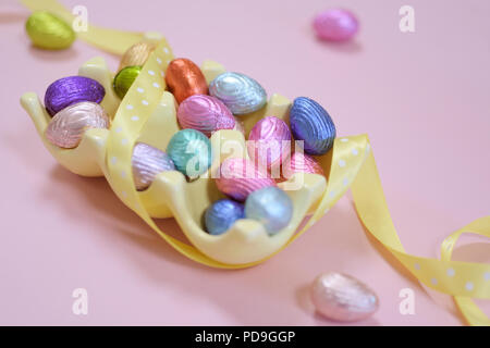 colourful chocolate Easter eggs in a yellow egg box with yellow ribbon and pink background Stock Photo