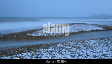 Blurred sea waves on a pebble beach covered in snow near town of Seaton in Devon Stock Photo