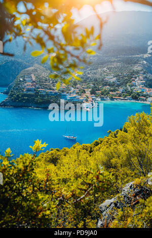 Assos village, Kefalonia. Greece. White yacht in blue bay framed by nature. Turquoise colored bay in Mediterranean sea surrounded by pine trees under bright sun beam light Stock Photo