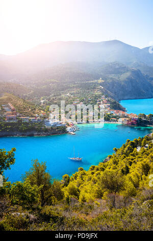 Assos village in morning light, Kefalonia. Greece. White lonely yacht in beautiful turquoise colored bay lagoon water surrounded by pine and cypress trees along the coastline Stock Photo