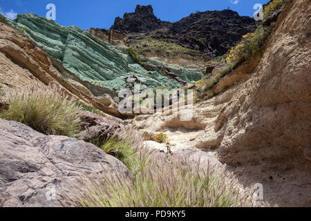 Turquoise colored rock layer Los Azulejos De Veneguera, volcanic rock steeped in sodium iron silicate, at Mogan, Lamprey grass Stock Photo