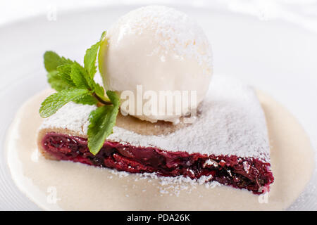 berry strudel cake served with ice cream, mint leaf and vanilla sauce. Classical austrian dessert on white plate. Sweet dessert in the restaurant. Morning light. Stock Photo
