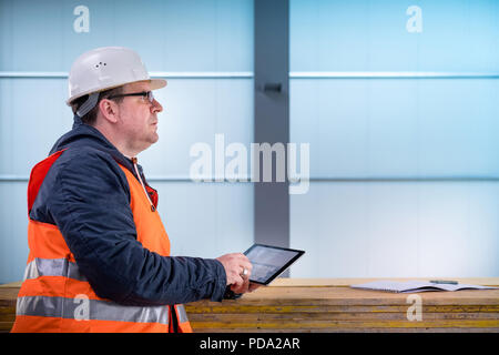Portrait of development supervisor wearing protective vest and helmet proofing blueprints using a digital tablet inside unfinished building Stock Photo