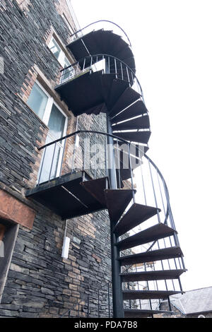 Looking up to sky from under a circular, metal fire escape on four storey town centre stone built flats in Keswick, Cumbria,UK Stock Photo