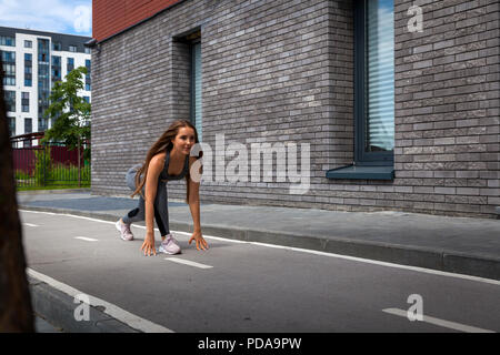 A young athletic woman stands in a low start for running in the stadium on a summer day , in a modern urban courtyard Stock Photo