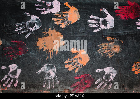 Colorful palm prints on black painted concrete wall, abstract background texture Stock Photo