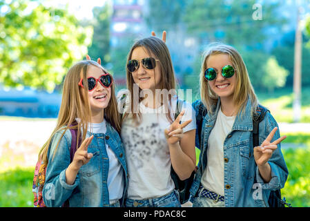 Three girls schoolgirl teenager, wearing jeans clothes and sunglasses. Happy smiling with gesture of hands showing Hello. Emotions of happiness and relaxation. The concept is best school friends. Stock Photo
