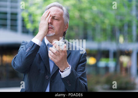 Desperate businessman holding his cell phone Stock Photo
