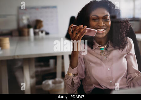 Businesswoman in formal attire talking over mobile phone on loudspeaker sitting at home. Woman entrepreneur managing business from home discussing wor Stock Photo