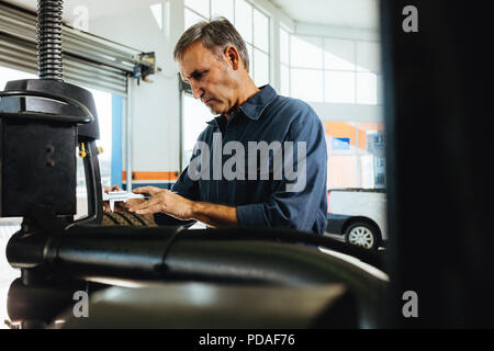 Mechanic checking the car wheel surface on machine. Technician working in automobile tyre mounted on machine in garage. Stock Photo