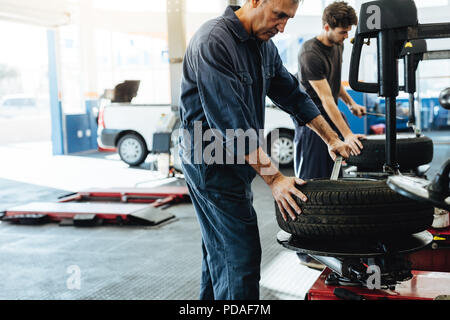 Mechanics working in car repair workshop. Auto repair workers working on tire replacing machine in auto repair shop. Stock Photo