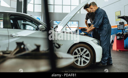 Automobile technicians using electronic diagnostic equipment to tune a car. Mechanics using a device to check the engine. Stock Photo