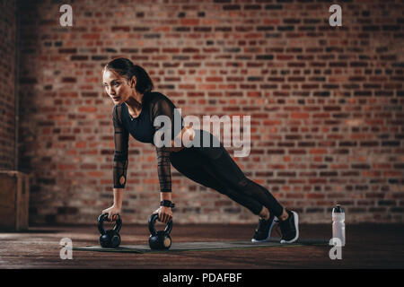 fitness woman doing pushups with kettle bell at gym. Female athlete doing cross training at gym. Stock Photo