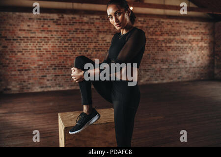 Portrait of fit young sports female stretching her leg at gym. Young woman doing stretching workout at fitness studio. Stock Photo