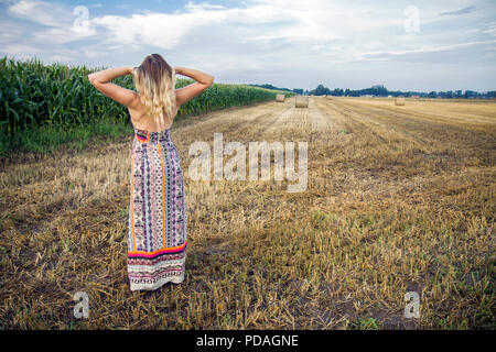 Blonde girl in a long dress standing in the corn field. Stock Photo