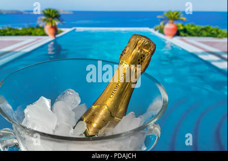 LUXURY VACATION Champagne bottle on ice, chilling in crystal glass wine cooler on terrace with luxury vacation infinity pool and sea coast view behind Stock Photo