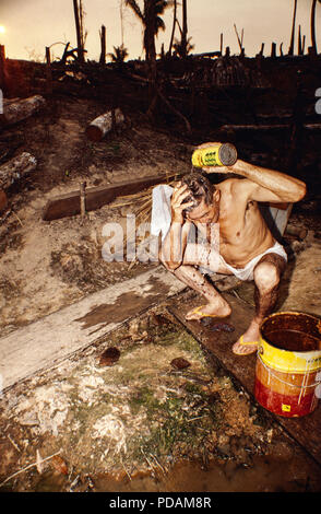 Degrading labor, man washes himself using a can of water at the end of a tough working day clearing the forest, Amazon deforestation. Acre State, Brazil. Stock Photo