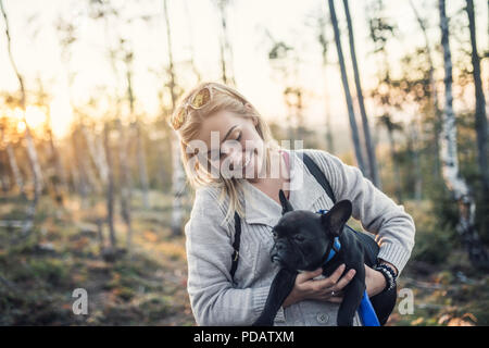 Young blond woman enjoying with her french bulldog puppy in sunny day. Stock Photo