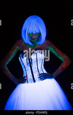 concept of wedding photosession in neon lighting in vogue style bride holds hands on the waist and glows in the dark young girl with hairstyle quads and bouquet posing in white wedding dress under the UV rays on a dark background in the studio Stock Photo