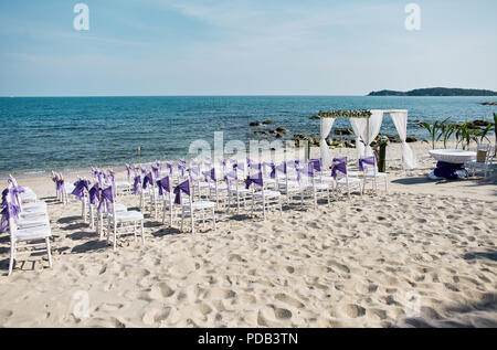 Beach wedding venue settings on the white sand at seaside with white chiavari chairs decorating with violet organza sash, minimal flower decoration, p Stock Photo