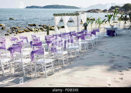 Beach wedding venue settings on the white sand at seaside with white chiavari chairs decorating with violet organza sash, minimal flower decoration, p Stock Photo