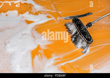 Brush leaving strokes in white foam and soap on yellow car washed in carwash. Stock Photo