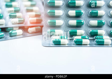 Green-white small capsule pills in blister packs on white table and blurred background of pills pack. Vitamins and supplements. Health care concept. P Stock Photo